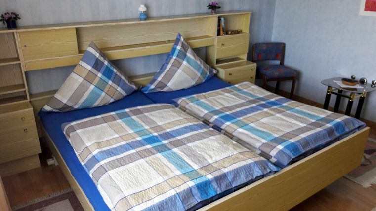 Een gezellige slaapkamer met een tweepersoonsbed en geruite dekens. Het meubilair is van licht hout en de ruimte ziet er uitnodigend uit.