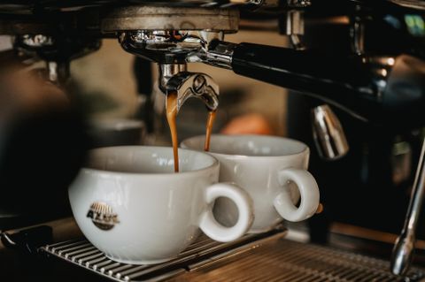 Zwei weiße Kaffeetassen stehen unter einer Espressomaschine. Frischer Espresso fließt aus dem Auslauf.