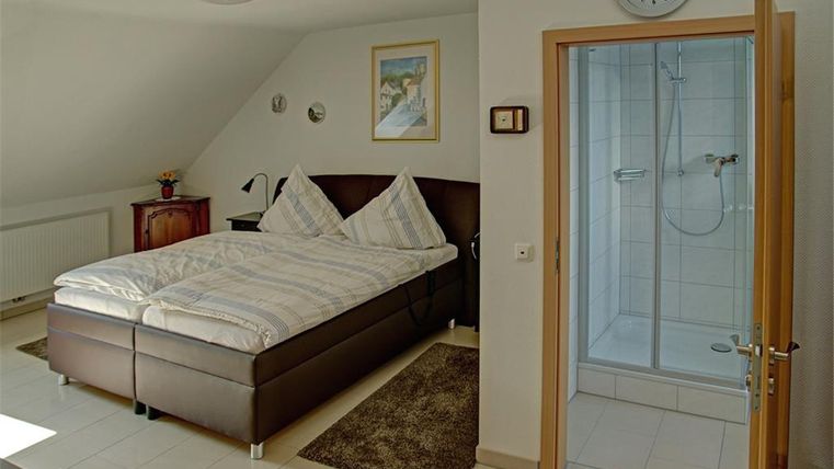 Ein modernes Schlafzimmer mit einem Doppelbett und einer Dusche in der Ecke. Der Raum ist hell und gemütlich eingerichtet.