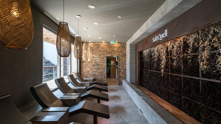 Ein eleganter Wellnessbereich mit bequemen Liegen und einer Steinwand. Sanftes Licht und natürliche Materialien schaffen eine entspannende Atmosphäre.