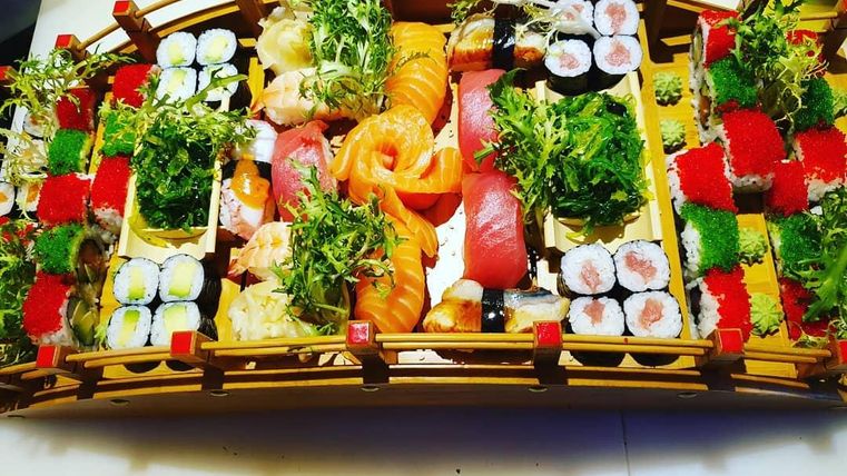 Ein kunstvoll dekoriertes Sushi-Arrangement auf einem Holztablett. Es umfasst verschiedene Sushi-Sorten mit frischen Zutaten und farbenfrohen Beilagen.