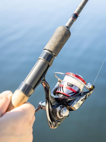 Een hand houdt een hengel met een moderne molen. Op de achtergrond is rustig water te zien.