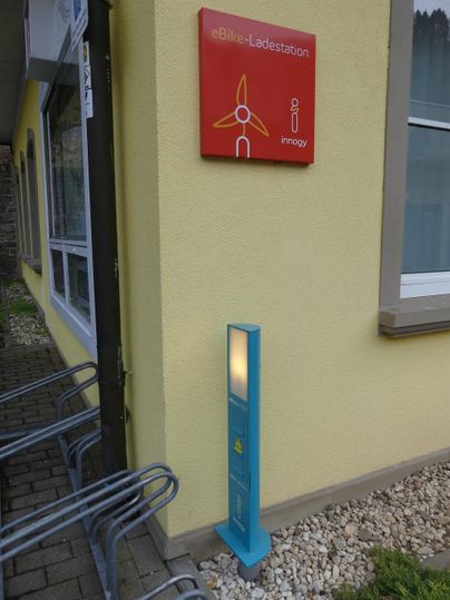 An information sign on a yellow wall, next to a blue object. The area is designed with gravel and there are some bike racks nearby.