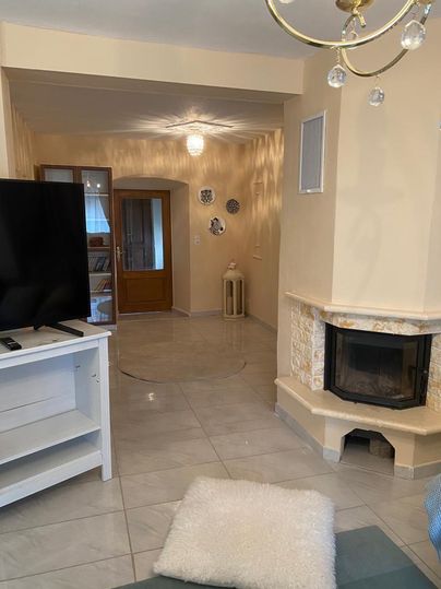 Ein heller Wohnraum mit einem modernen Fernseher und einem gemütlichen Kamin. Die Wände sind in sanften Farben gehalten und es gibt einen einladenden Eingang.