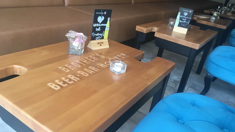 Ein gemütlicher Innenraum mit Holztischen und blauen Stühlen. Auf den Tischen stehen kleine Blumenvasen und Menükarten.