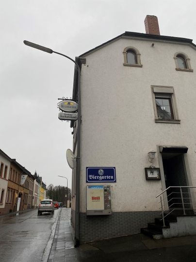 Een gebouw aan een straat met een blauw teken dat op een accommodatie wijst. Het weer is bewolkt en er staat een auto op de straat.