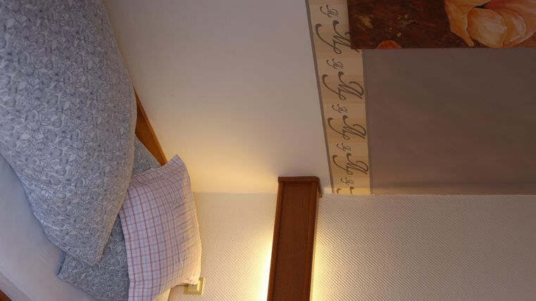 Ein gemütliches Schlafzimmer mit einem weichen Bett und dekorativen Kissen. An der Wand hängt ein schönes Kunstwerk mit einer Blume.