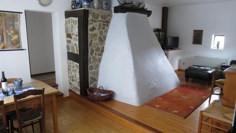 Een gezellige kamer met een houten vloer en een witte hahoek. Er is een eettafel, stoelen en een bank in de hoek.