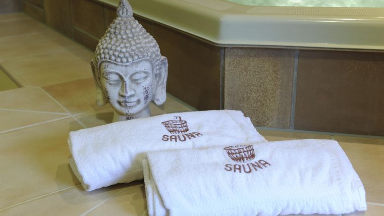 Ein entspannender Wellnessbereich mit zwei weißen Handtüchern und einer Buddha-Skulptur. Der Hintergrund zeigt einen Whirlpool, der zur Erholung einlädt.