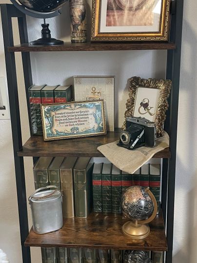 Een boekenplank met oude boeken, decoratieve voorwerpen en een wereldbol. Hieronder zijn een ingelijste foto en een oude camera te zien.