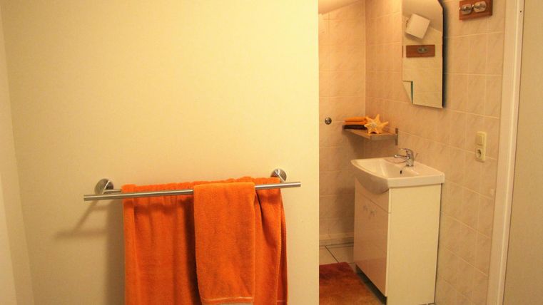 A bright bathroom with white walls and tiles. An orange towel hangs on the wall, and there is a small washbasin with a mirror.