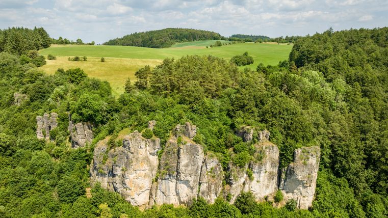 Een indrukwekkende rotsformatie omringd door weelderig groen en zachte heuvels. De lucht is gedeeltelijk bewolkt en geeft het landschap een vredige sfeer.