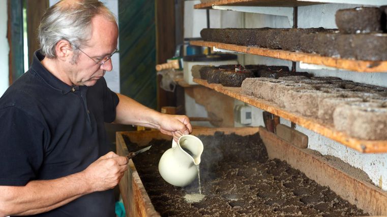 Ein Mann gießt Wasser auf Erde in einem Holzregal. Im Hintergrund sind gepresste Erdballen zu sehen.
