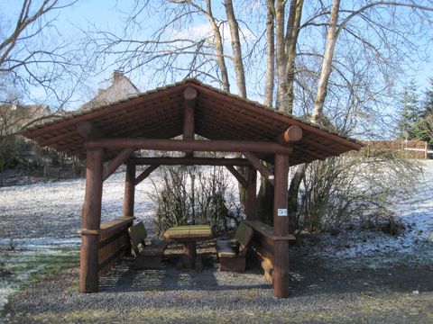 Holzschutzhütte mit Tisch und Bänken, umgeben von kahlen Bäumen und leichtem Schneefall auf dem Boden.