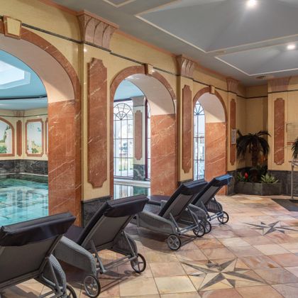 Een elegante binnenswembad met comfortabele ligstoelen en stijlvolle pilaren. De sfeer is ontspannend en uitnodigend.