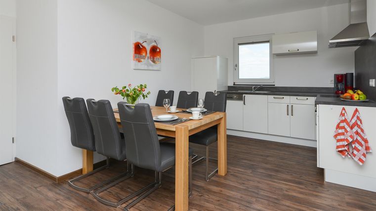 Eine moderne Küche mit einem Essbereich und einem Holztisch. Sechs Stühle sind um den Tisch gruppiert, und frische Blumen sind als Dekoration vorhanden.