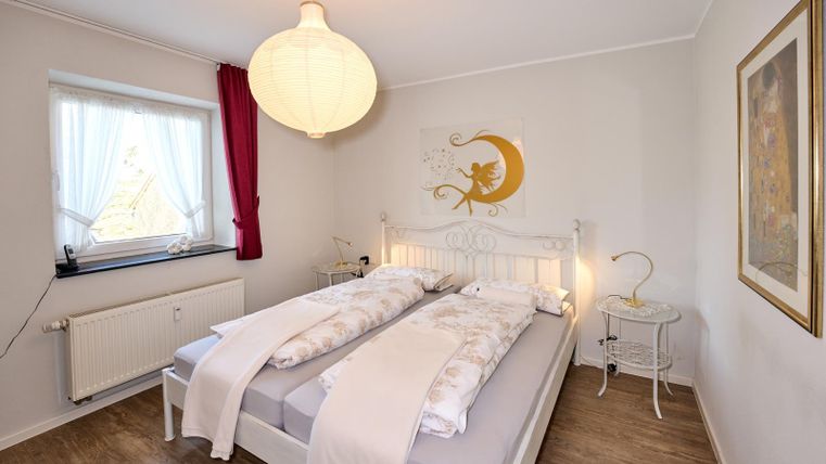 Een lichte slaapkamer met een tweepersoonsbed en moderne verlichting. De muren zijn in zachte kleuren en een groot raam zorgt voor veel daglicht.