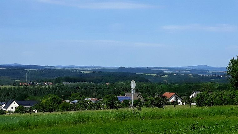 A vast landscape with gentle hills and scattered houses. The sky is clear and blue, ideal for a relaxing day outdoors.