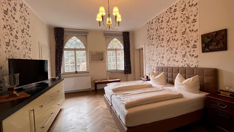 Ein elegantes Schlafzimmer mit einem großen Bett und schönen Fenstern. Die Wände sind mit einer stilvollen Tapete dekoriert.