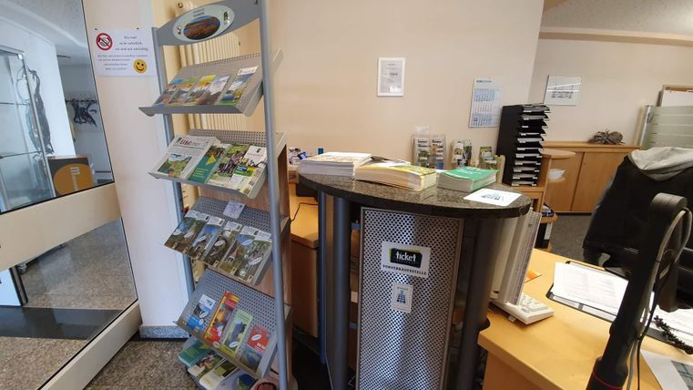 Ein Empfangsbereich mit einem Informationsständer für Broschüren und einem Schreibtisch. Die Umgebung ist hell und freundlich gestaltet.