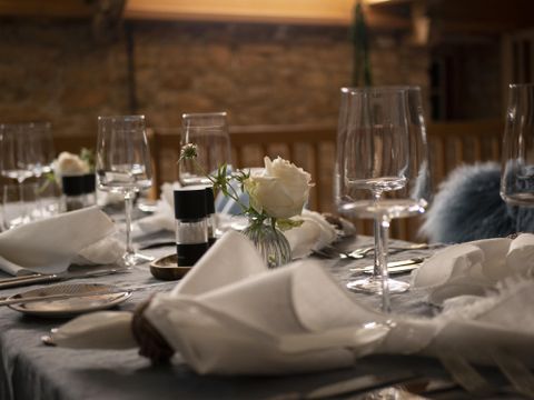 Ein elegant dekorierter Tisch mit Gläsern und Servietten. In der Mitte steht eine Blumenvase mit einer weißen Rose.