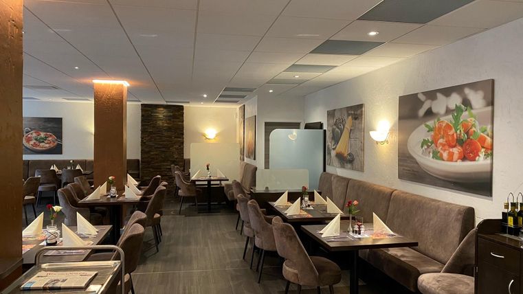 Elegantes Restaurant mit gedeckten Tischen, braunen Stühlen und Wandbildern von Speisen. Dezente Beleuchtung und moderne Einrichtung.