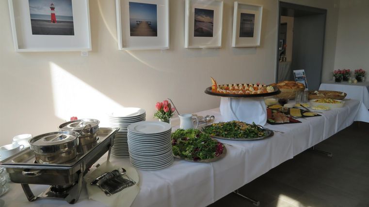 A laid table with various foods and drinks. In the background, pictures hang on the wall.
