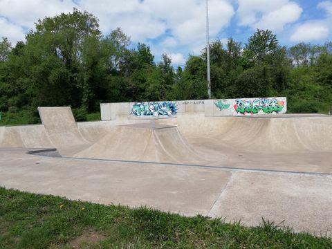 Een skatepark met verschillende betonnen rampen. Op de achtergrond zijn bomen en graffiti-muren te zien.
