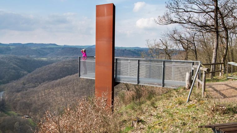 Ein Aussichtsplattform über einer landschaftlich reizvollen Aussicht. Im Hintergrund sind Hügel und bewaldete Flächen zu sehen.