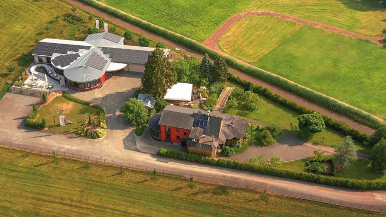 Een modern gebouw in een landelijke omgeving omringd door weiden en bomen. Het complex heeft een geplaveide toegang en een groot grasveld.