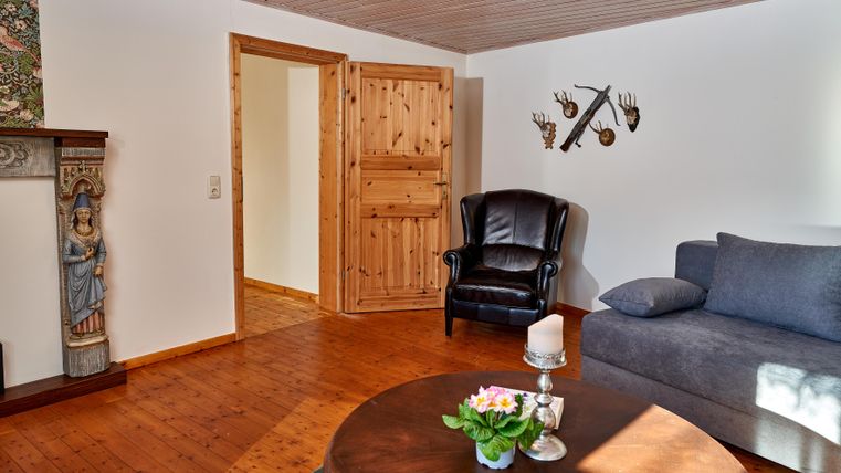 A cozy living room with a black armchair, a gray sofa, and a round table. The warm wood paneling and decorative elements give the room an inviting character.