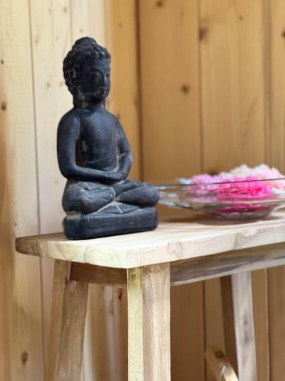 Eine Buddha-Statue aus schwarzem Material auf einem Holztablett. Daneben befindet sich eine Schüssel mit buntem Dekorationsmaterial.