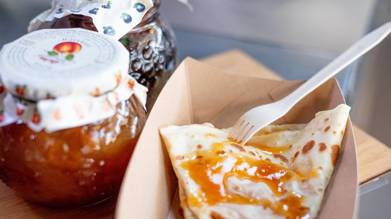 Een heerlijke crêpe met jam op een papieren bord. Daarnaast staan twee glazen jam.