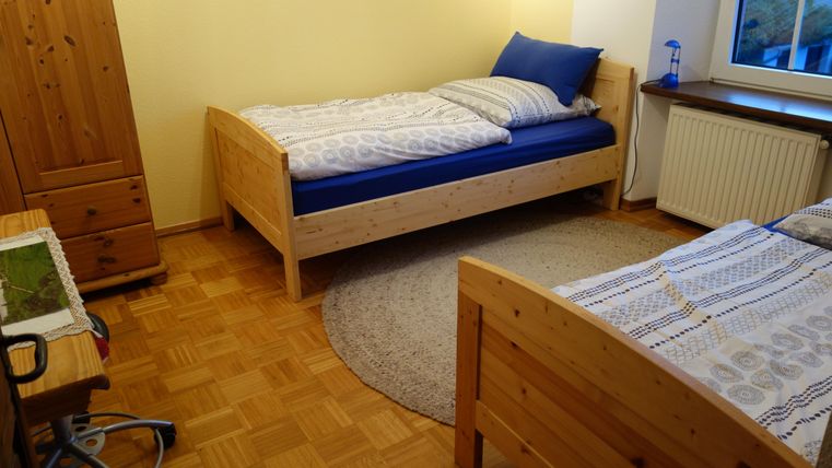 Een eenvoudige slaapkamer met twee bedden en een rond tapijt. De muren zijn geel geschilderd, en de kamer lijkt helder en uitnodigend.