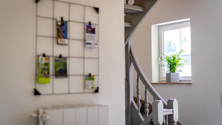 Ein einladender Flur mit einer Treppe und einem Fenster. An der Wand hängt ein Gitter für Notizen und Broschüren.