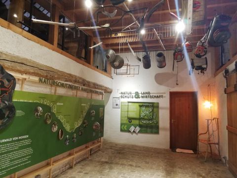 Ein Innenraum mit einer informativen Wandgestaltung über Naturschutz. Verschiedene Geräte hängen von der Decke und es gibt grüne Elemente auf den Wänden.