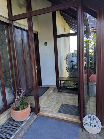 Een uitnodigende entree met grote ramen en een kleine tafel. Op de voorgrond staat een bloempot en een tapijt op de vloer.