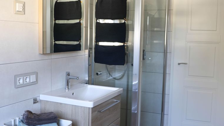 A modern bathroom with a shower, a sink, and a mirror. Towels are ready in a white basket.