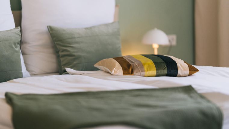 Een gezellig bed met groene en kleurrijke kussens. Het rustige kleurenpalet creëert een ontspannen sfeer.