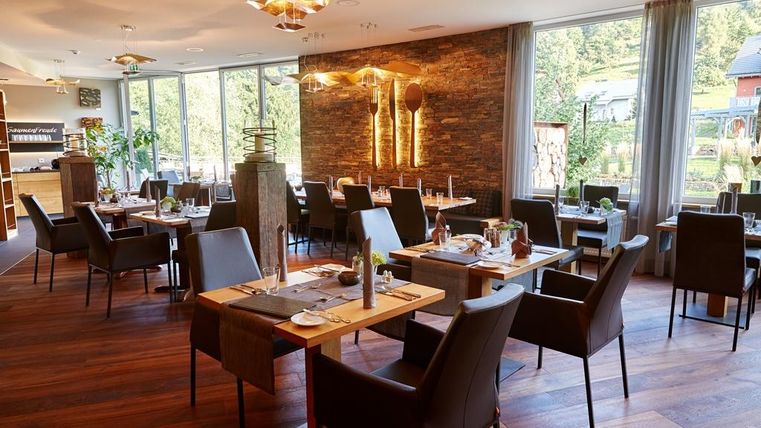 Een elegant restaurant met moderne tafels en stoelen. Grote ramen bieden uitzicht op de natuur.