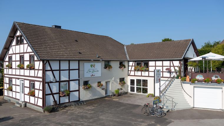 A modern half-timbered house with a terrace and flower windows. There is a clear blue sky and a small bike rack.