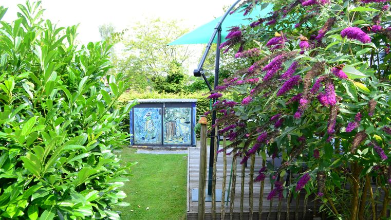 A friendly garden with lush greenery and colorful flowers. In the background, decorative artworks are visible.