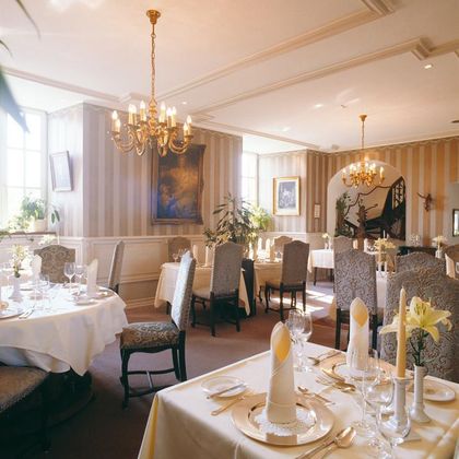 An elegant restaurant with beautifully set tables and stylish chairs. The warm colors and decorative elements create an inviting atmosphere.