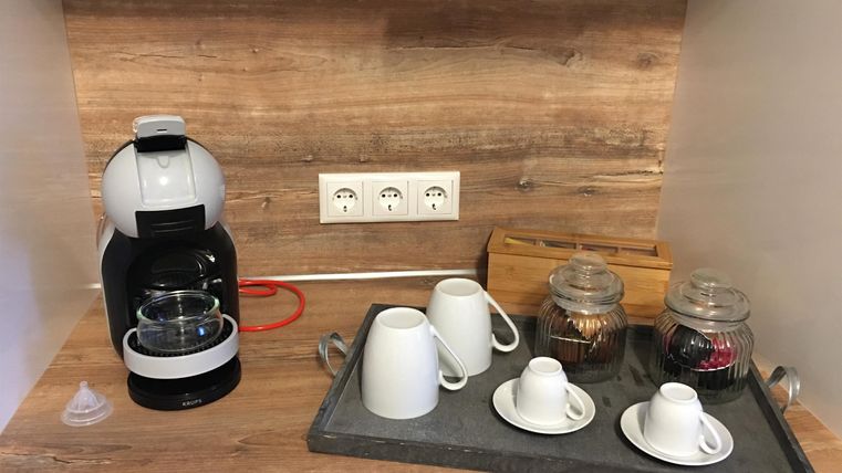 Eine moderne Kaffeemaschine steht auf einer Holzablage. Darunter sind verschiedene Tassen und Gläser mit Zutaten für Kaffee.