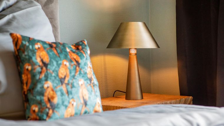Ein gemütliches Schlafzimmer mit einem dekorativen Kissen und einer stilvollen Lampe auf einem Nachttisch. Die warmen Farben schaffen eine einladende Atmosphäre.