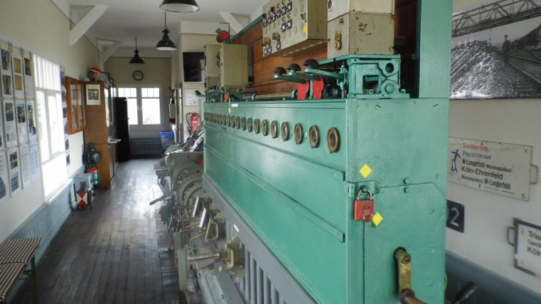 Historisches Stellwerk mit grünen Hebeln und Schaltern, Holzboden und Wänden mit Fotos und Schildern dekoriert.