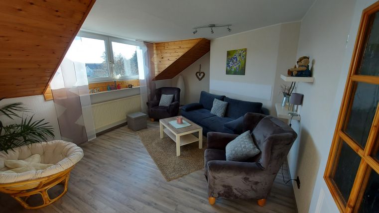 A cozy living room with a seating area and a bright window. The decor is modern and inviting, with a rug and plants.