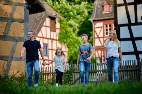 Een gezin wandelt door een pittoresk dorp met traditionele vakwerkhuizen. De kinderen houden elkaars handen vast en genieten van de dag op buiten.