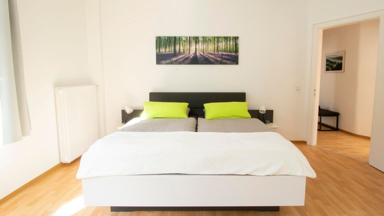 Ein modernes Schlafzimmer mit einem großen Bett und grünen Kissen. An der Wand hängt ein Bild von einem Wald.