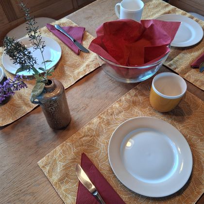 Ein gedeckter Tisch mit weißen Tellern, bunten Tassen und dekorativen Servietten. In der Mitte steht eine Schüssel und eine kleine Vase mit Blumen.